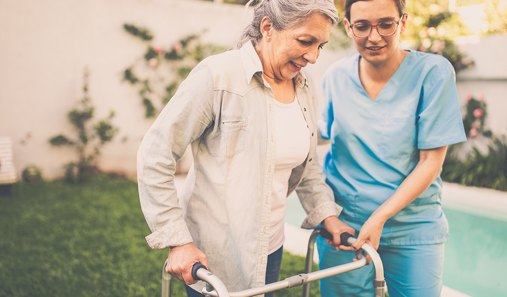 Caregiver helping senior woman using walker outside