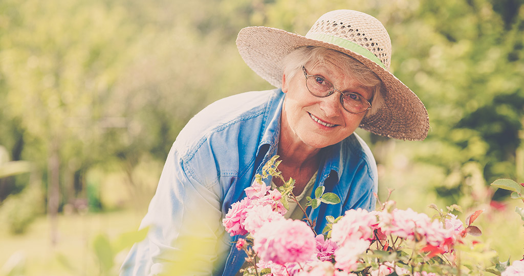 smiling elderly woman in garden with pink flowers