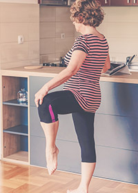 Woman exercising at home by lifting up leg and leaning against counter