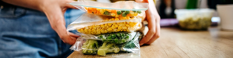 Person grabbing individually bagged corn, broccoli, and mixed vegetables