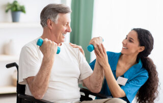 Female caregiver helping senior man in wheelchair lift weights