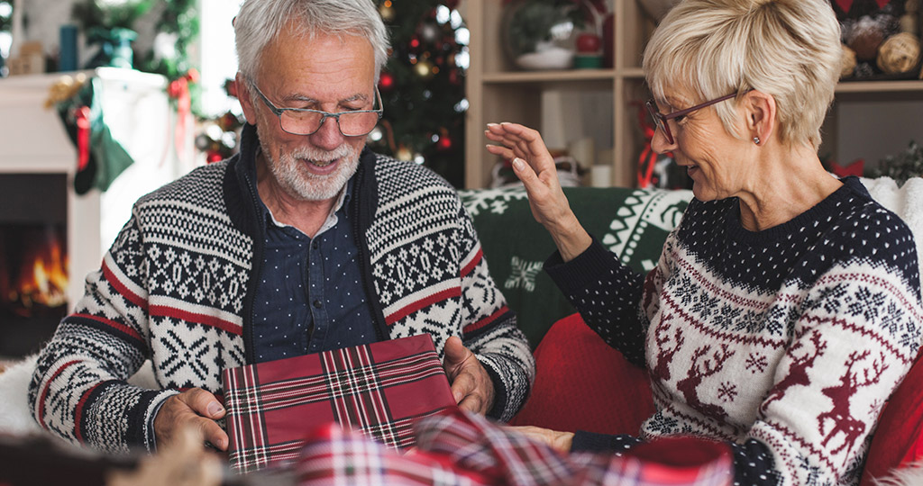 Senior couple wearing seasonal sweaters opening gifts