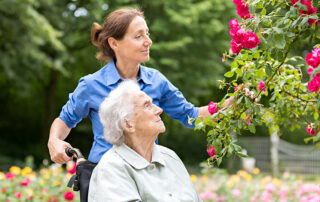 Female caregiver pushing happy woman in wheelchair through garden in the outdoors
