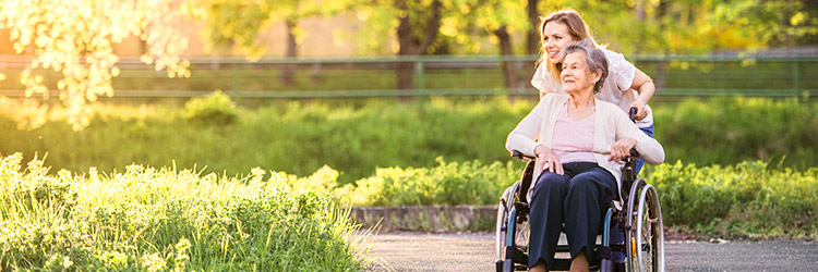 Smiling woman pushing elderly woman in wheelchair through park