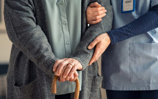 Caregiver helping woman holding cane walk