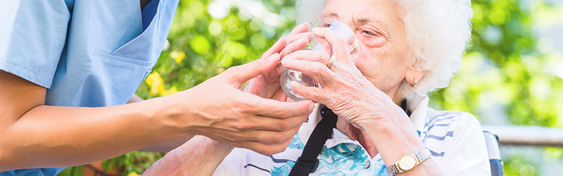 Caregiver handing elderly woman glass of water while sitting outside