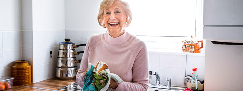 Smiling elderly woman drying dishes in kitchen