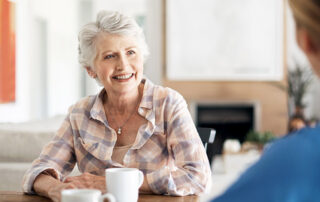 Smiling senior woman holding mug sitting at dining table with caregiver