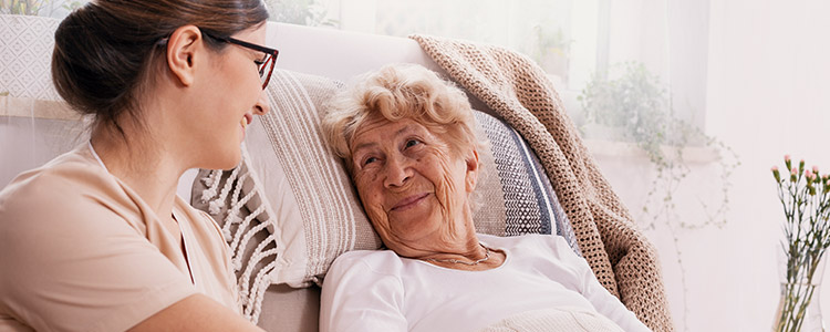 Senior woman resting in bed while talking with caregiver