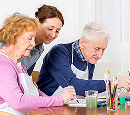Caregiver helping senior man and woman paint