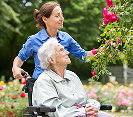 Senior in wheelchair being pushed through beautiful flower garden