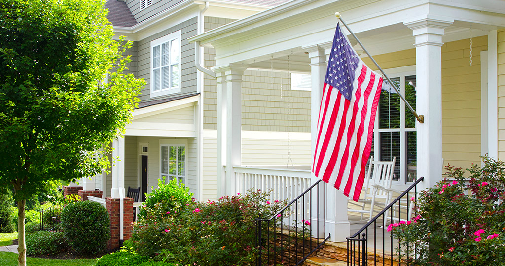 American flag hanging on the porch of a quaint bungalow home
