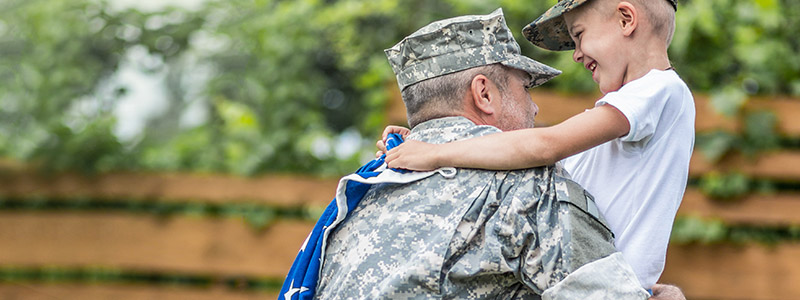 Smiling veteran hugging son holding American flag